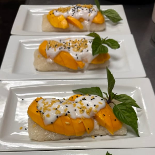 Three plates of mango sticky rice, topped with coconut cream, sesame seeds, and basil leaves.