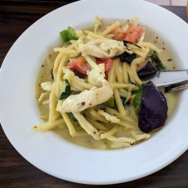 Thai green curry with chicken, bamboo shoots, tomatoes, and purple eggplant in a white bowl.