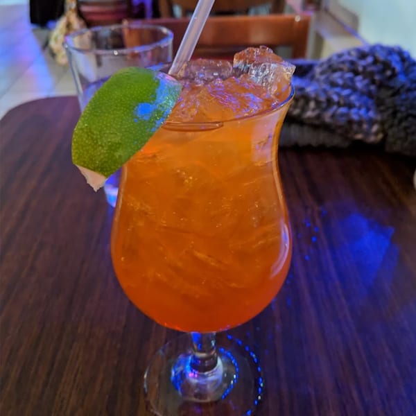 Orange cocktail with ice, a straw, and a lime wedge on a dark wooden table.