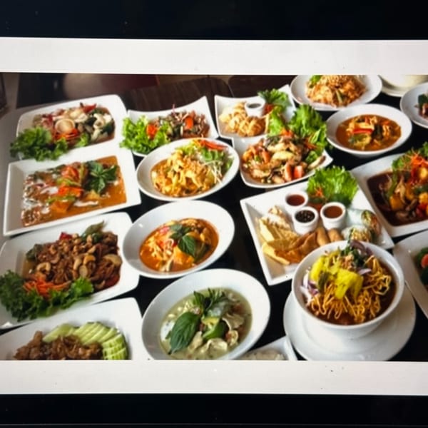 A large spread of various Thai dishes, including curries, noodles, and stir-fries, on a dark table.
