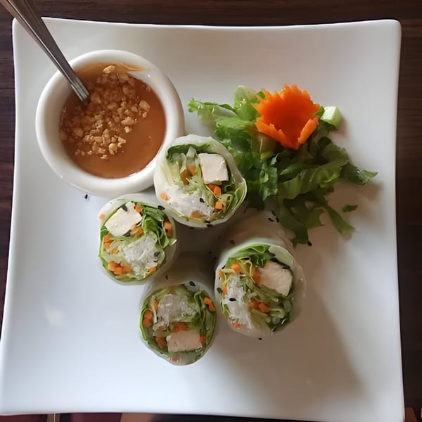 Four fresh spring rolls with tofu, lettuce, and carrots, served with peanut sauce and greens.