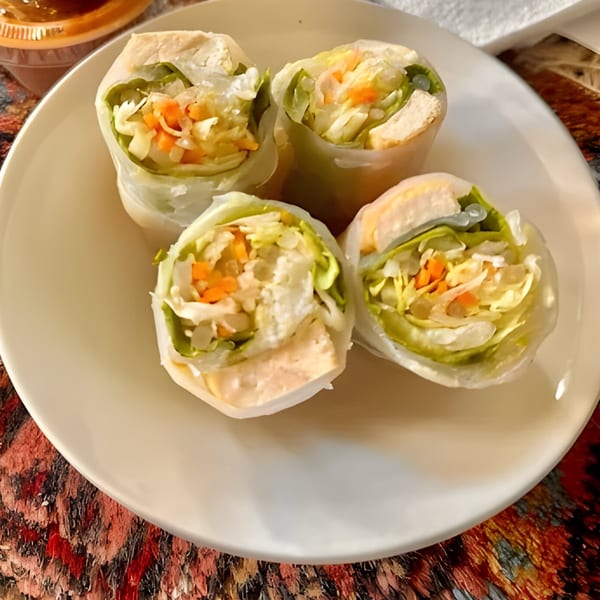 Four fresh Thai spring rolls filled with lettuce, carrots, and chicken on a white plate.