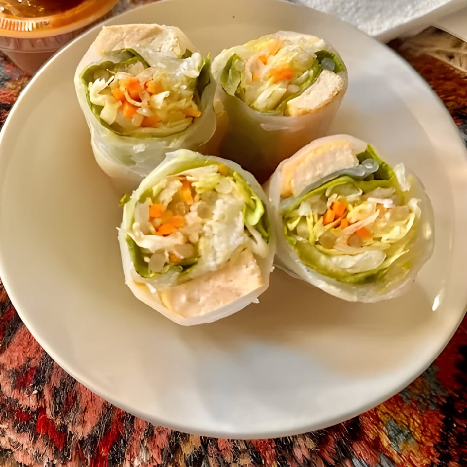 Four fresh Thai spring rolls filled with lettuce, carrots, and chicken on a white plate.