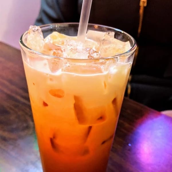 A tall glass of Thai iced tea with ice and a straw, on a dark wooden table.
