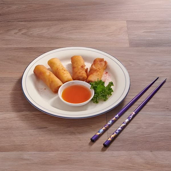 Four crispy Thai spring rolls with sweet chili sauce and lettuce on a white plate with purple chopsticks.