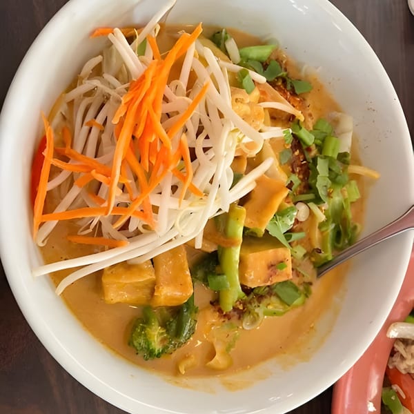 A bowl of Thai curry with tofu, broccoli, bean sprouts, and shredded carrots.