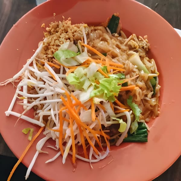 A vibrant Thai Chili Jam Pad See Ew with noodles, bean sprouts, carrots, and lettuce on an orange plate.