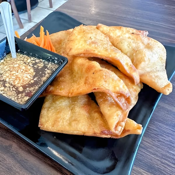 Crispy fried wontons with a side of peanut dipping sauce and shredded carrots on a black plate.